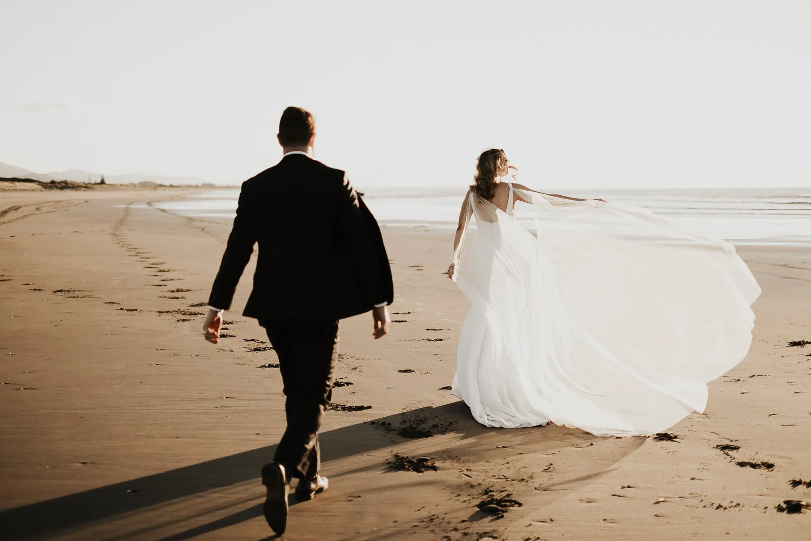Lucy and Hamish walking together along the beach on their wedding day.